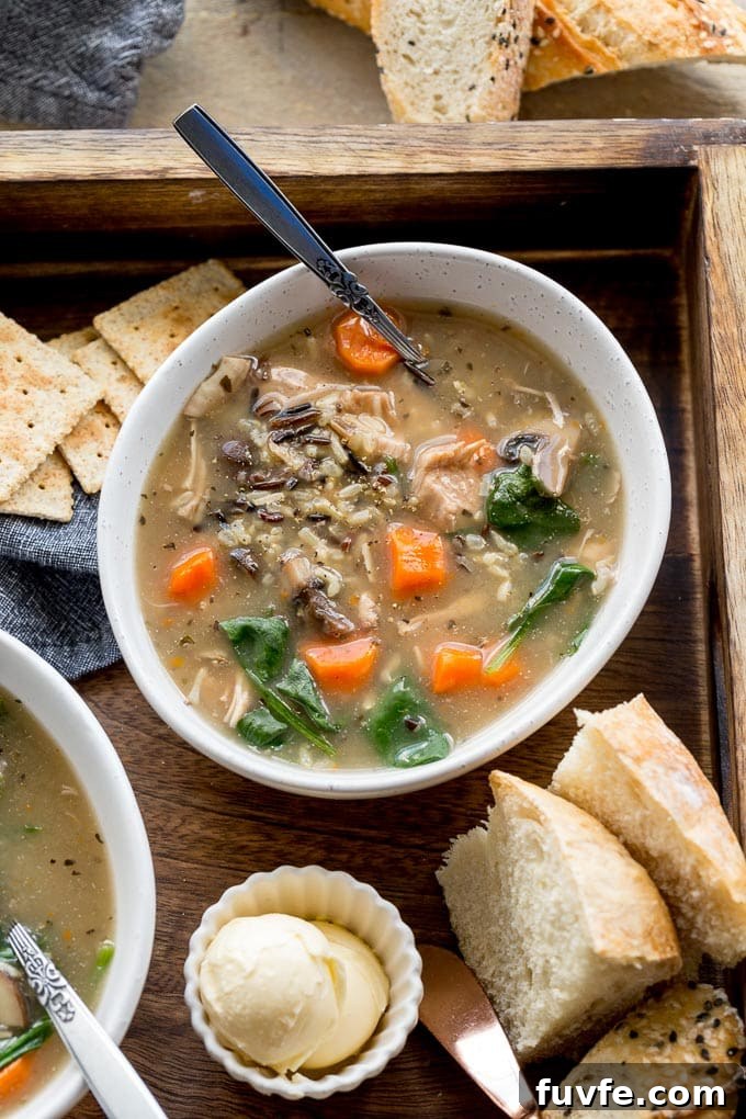 Overhead view of instant pot chicken wild rice soup in a white bowl on a wooden tray with bread and crackers.