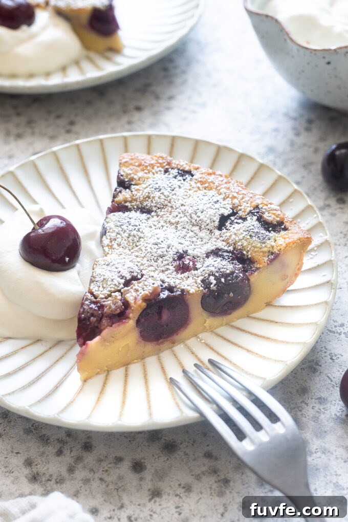 Slice of cherry clafoutis on a plate with whipped cream.