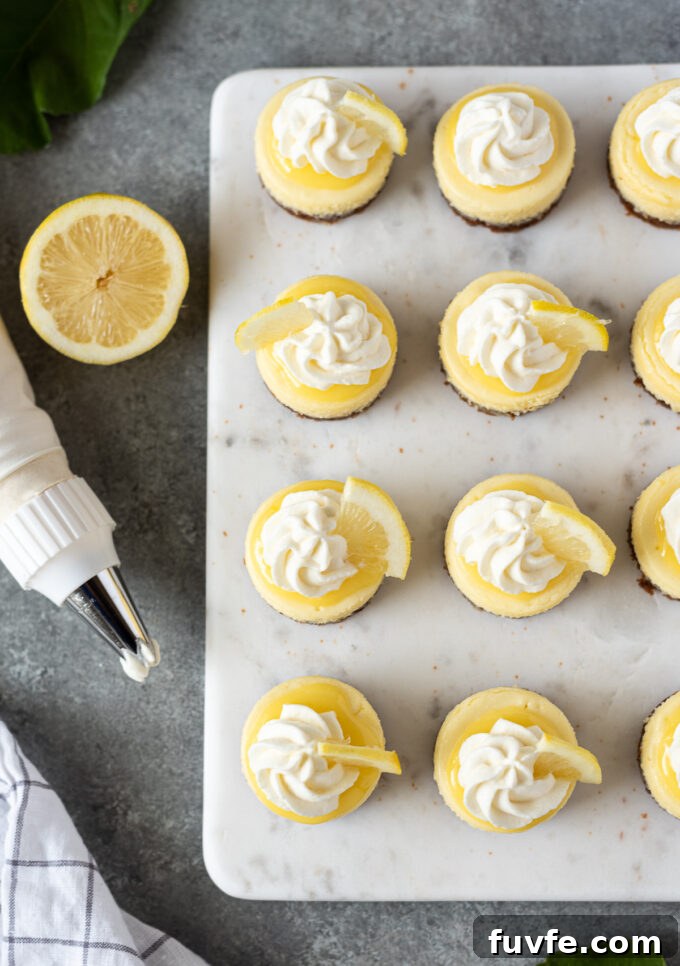 Mini lemon cheesecakes on a serving board with whipped cream and lemon slices.