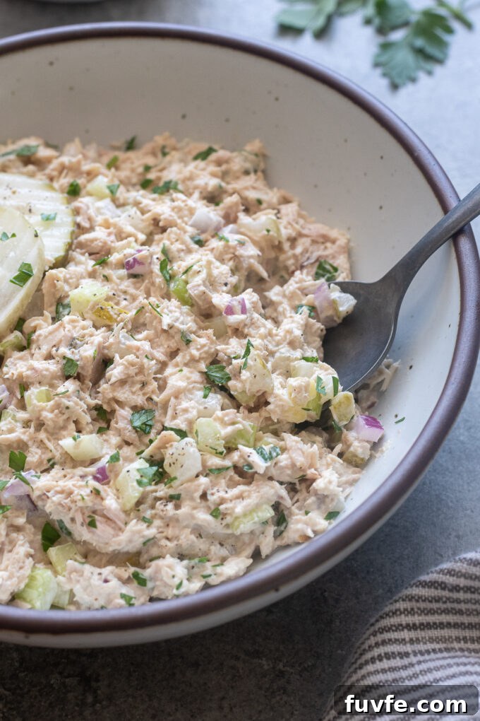 Tuna salad with pickles in a serving bowl with spoon digging in.