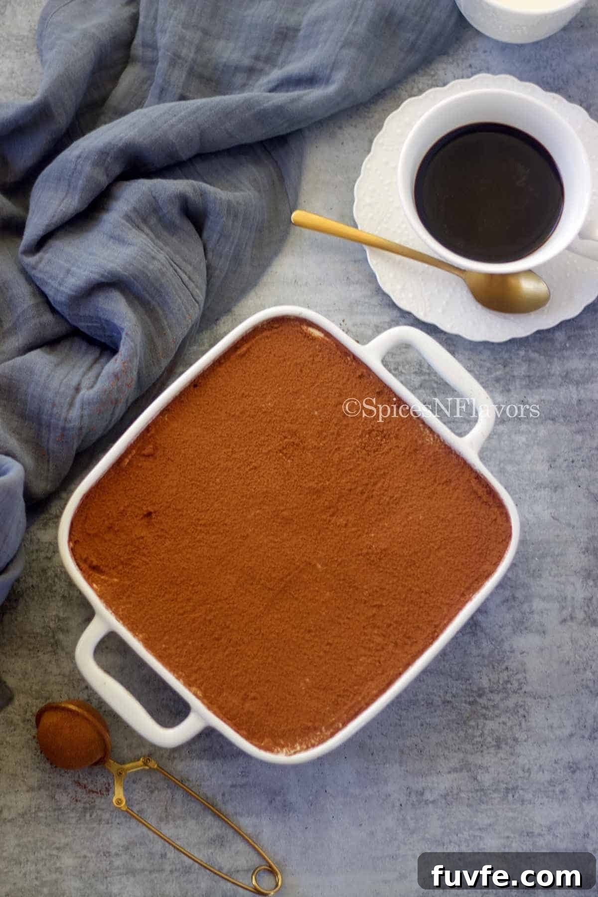 Eggless Tiramisu Recipe with Homemade Ladyfingers 9 assembled tiramisu in a white baking dish dusted with cocoa powder served with black coffee on the side