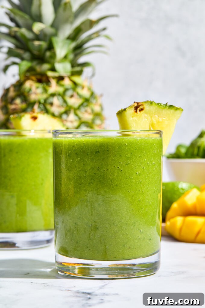 Kale fruit smoothie in a glass with pineapple wedge on rim.
