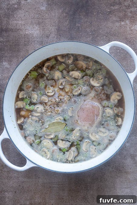 Broth, chicken and wild rice added to pot for chicken wild rice soup.