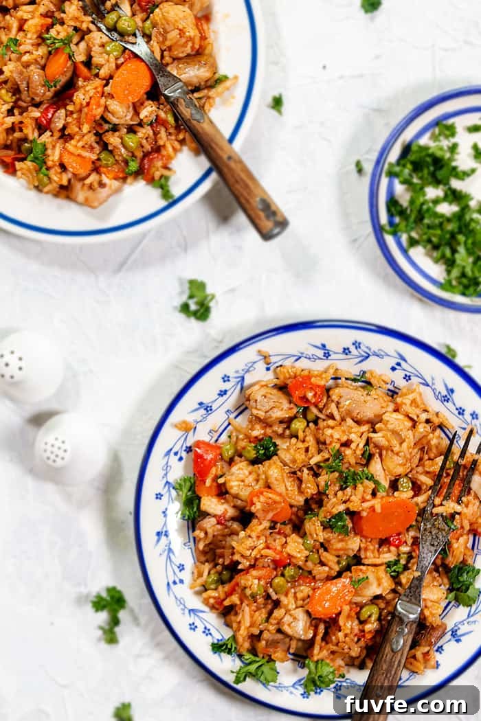 One-Pan Chicken and Rice with Garden Vegetables 5 Overhead of two plates with rice dish on a white tablecloth.