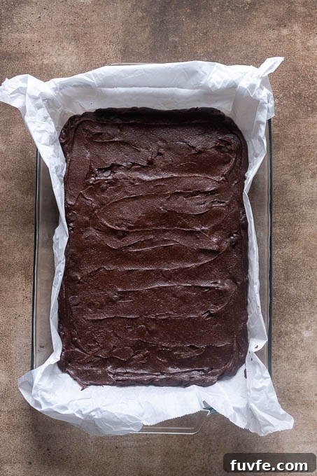 Unbaked cocoa brownies in baking dish with parchment paper.