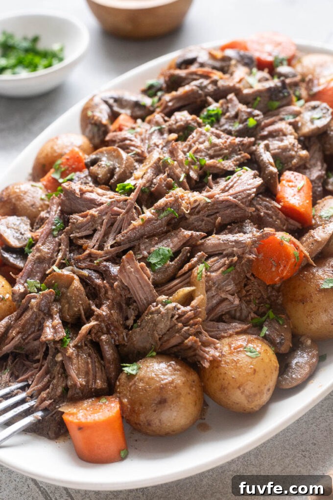 Chuck roast pot roast on a platter with potatoes, carrots and mushrooms.