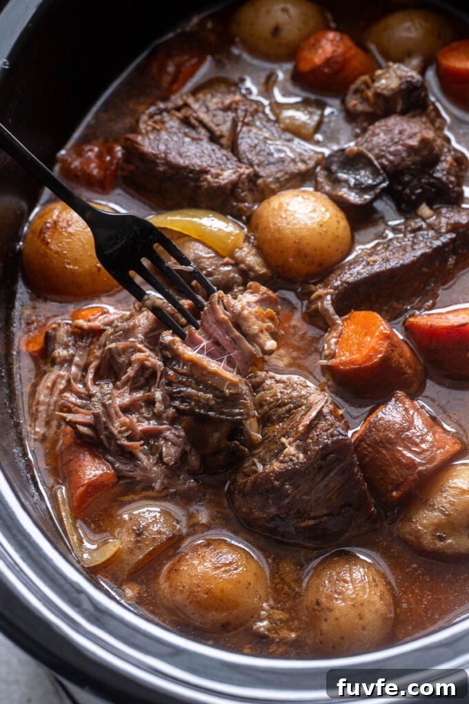 Fork shredding beef pot roast in the slow cooker.