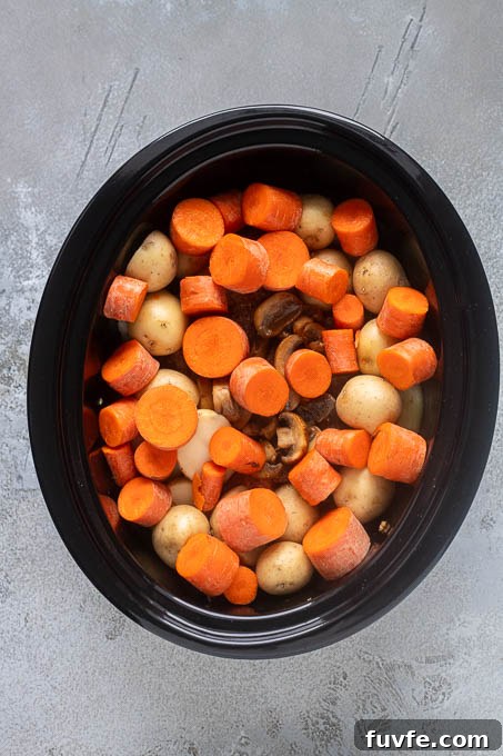 Potatoes and large chunks of carrots on top of pot roast before cooking.