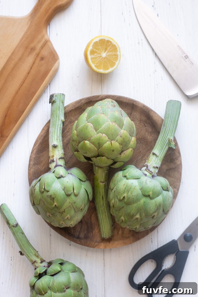 How to Cook Tender Instant Pot Artichokes 3 Ingredients needed to cook artichokes including fresh artichokes, lemon, garlic and bay leaf.