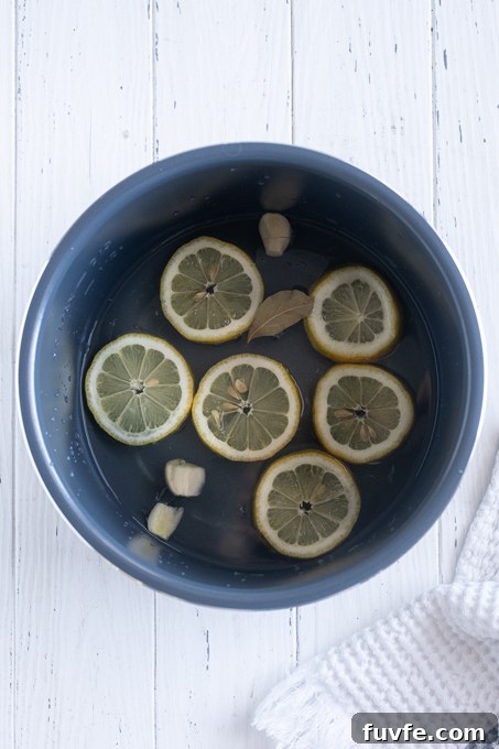 How to Cook Tender Instant Pot Artichokes 8 Water with lemon slices, garlic and bay leaf in bottom of Instant Pot.