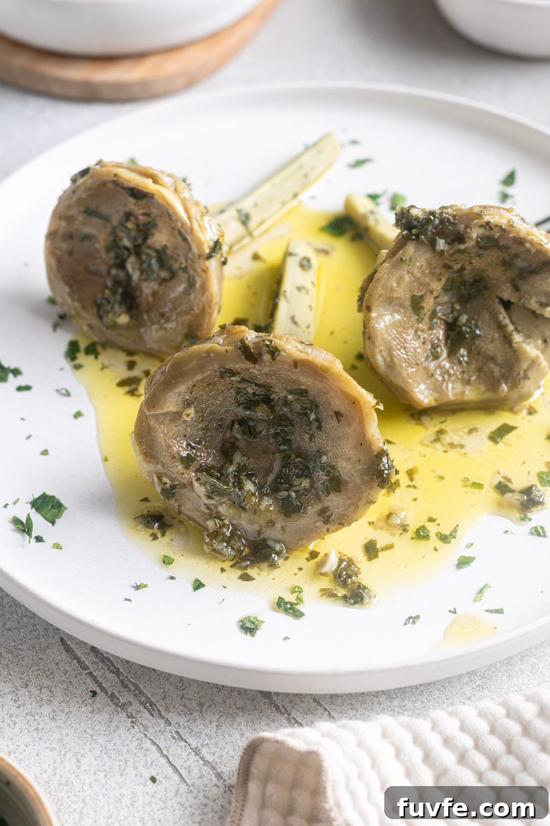 Italian braised artichokes on a plate with garlic herb olive sauce drizzled over.