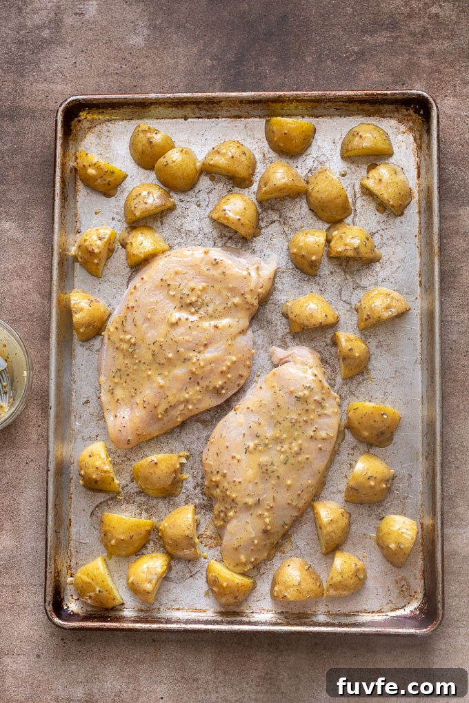 Chicken breast and potatoes brushed with honey mustard sauce on sheet pan.