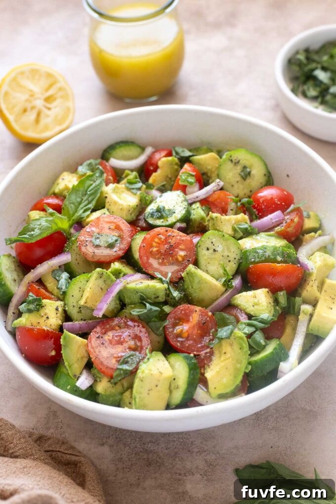 Cucumber tomato avocado salad in a bowl with basil and lemon vinaigrette.