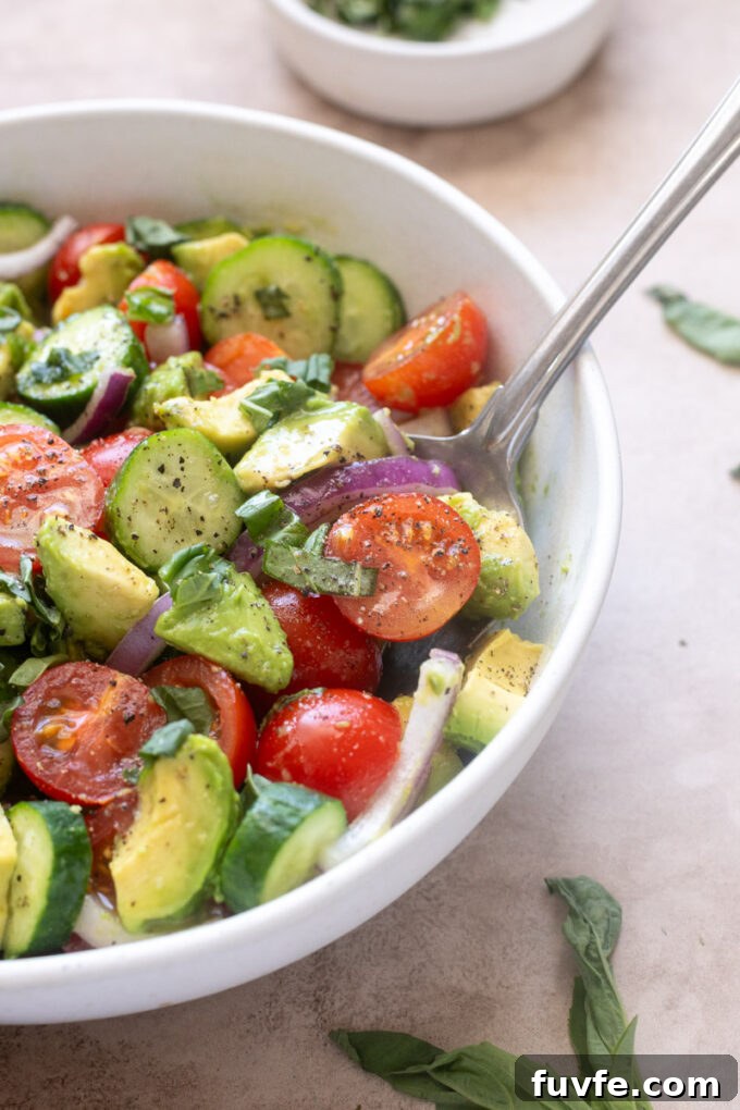 Cucumber tomato avocado salad with lemon vinaigrette in serving bowl with a spoon.
