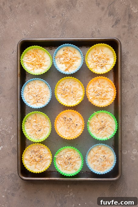 Blended egg and cottage cheese mixture in silicone muffin molds with grated cheese.