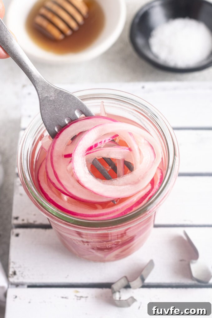 Fork pulling quick pickled red onions out of a jar.