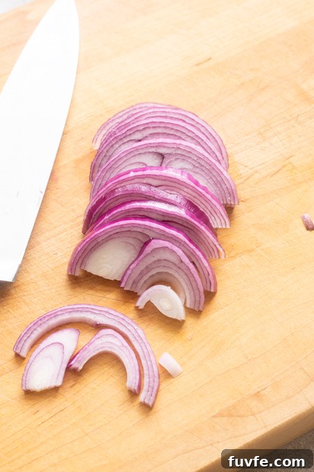Red onion sliced with a knife on a cutting board.
