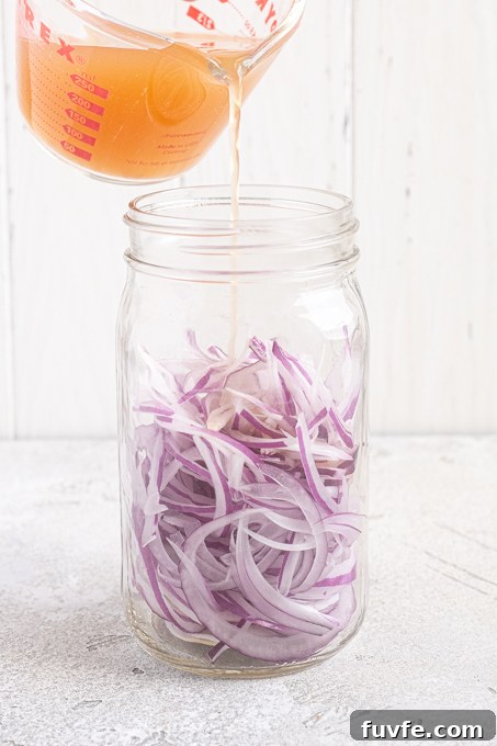 Sliced onions in jar with brine pouring over the top.