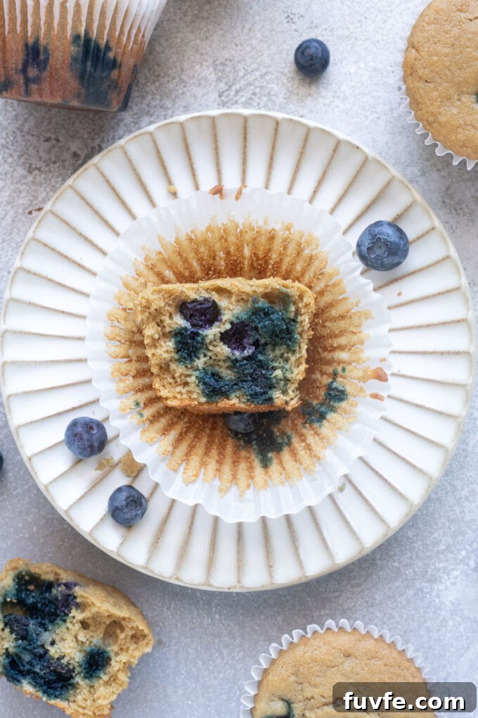 Fluffy blueberry oat flour muffin cut in half on a plate with blueberries.