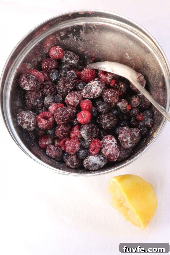 Berries in a mixing bowl with. spoon and half of a lemon beside it