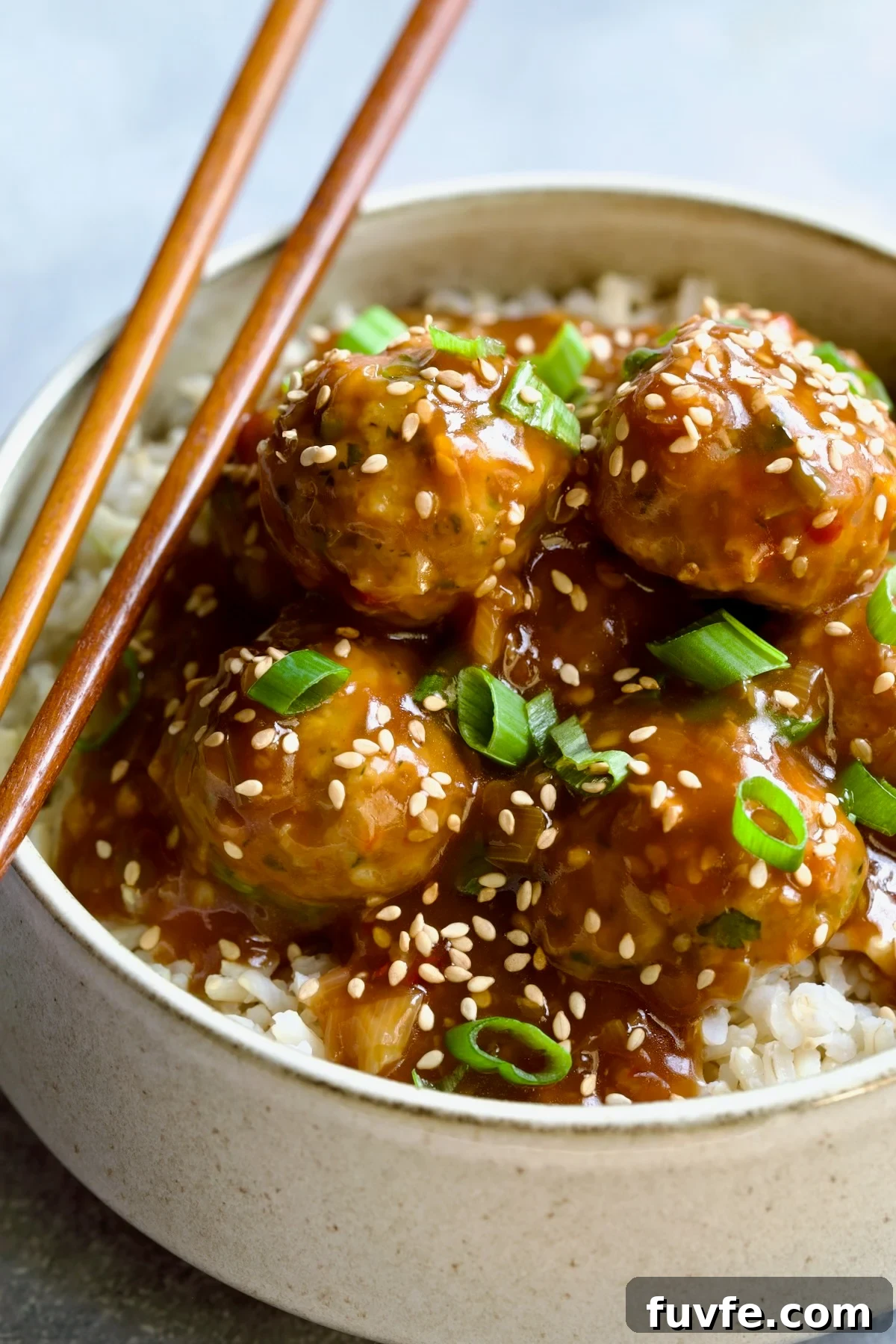 Asian-Style Turkey Meatballs with Ginger-Soy Glaze 14 Asian Turkey Meatballs in serving bowl with chopsticks garnished with sesame seeds and scallions over brown rice.