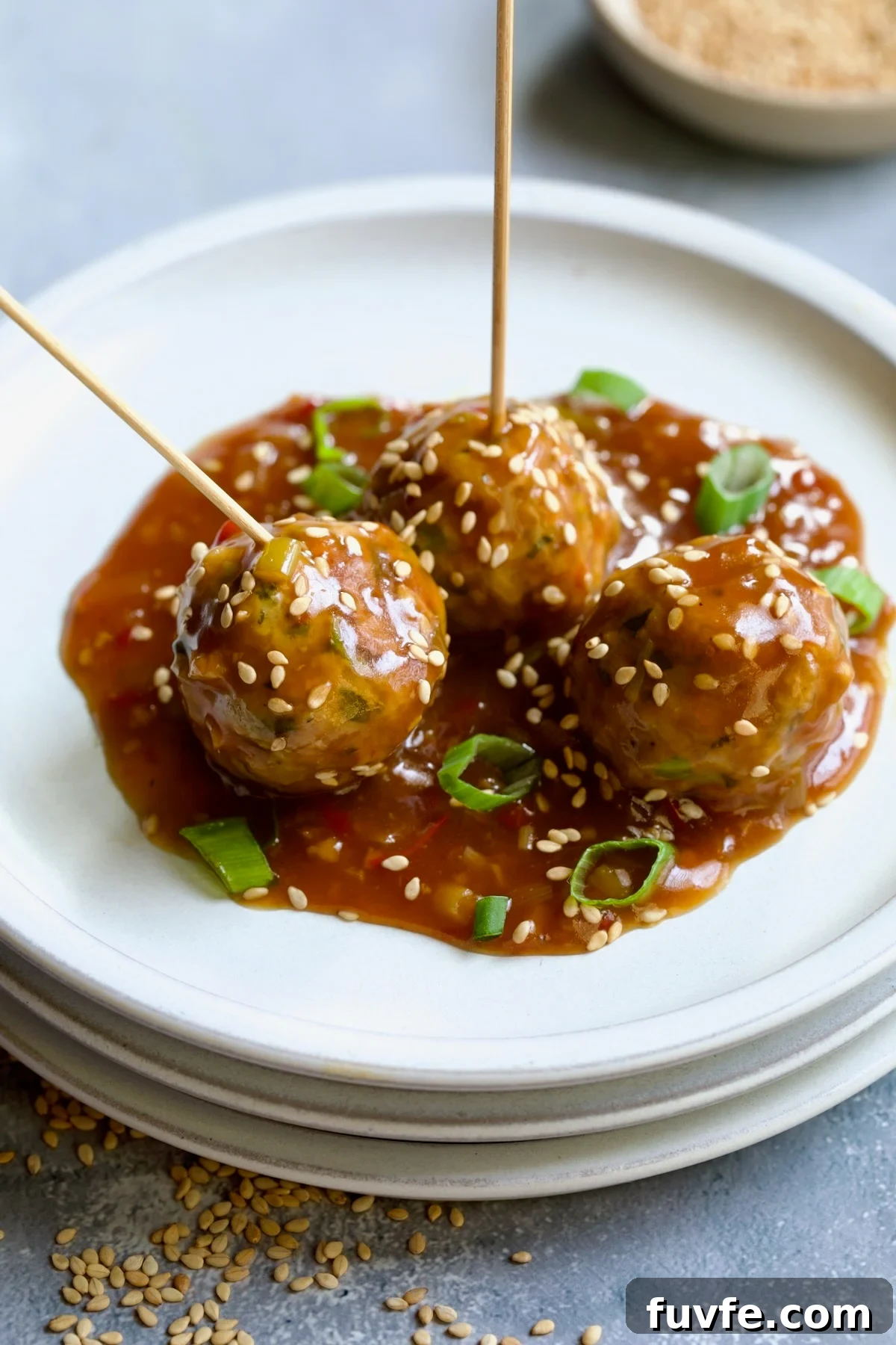 Asian-Style Turkey Meatballs with Ginger-Soy Glaze 15 Three Asian Turkey Meatballs on appetizer plates with serving picks inserted garnished with sesame seeds and scallions.