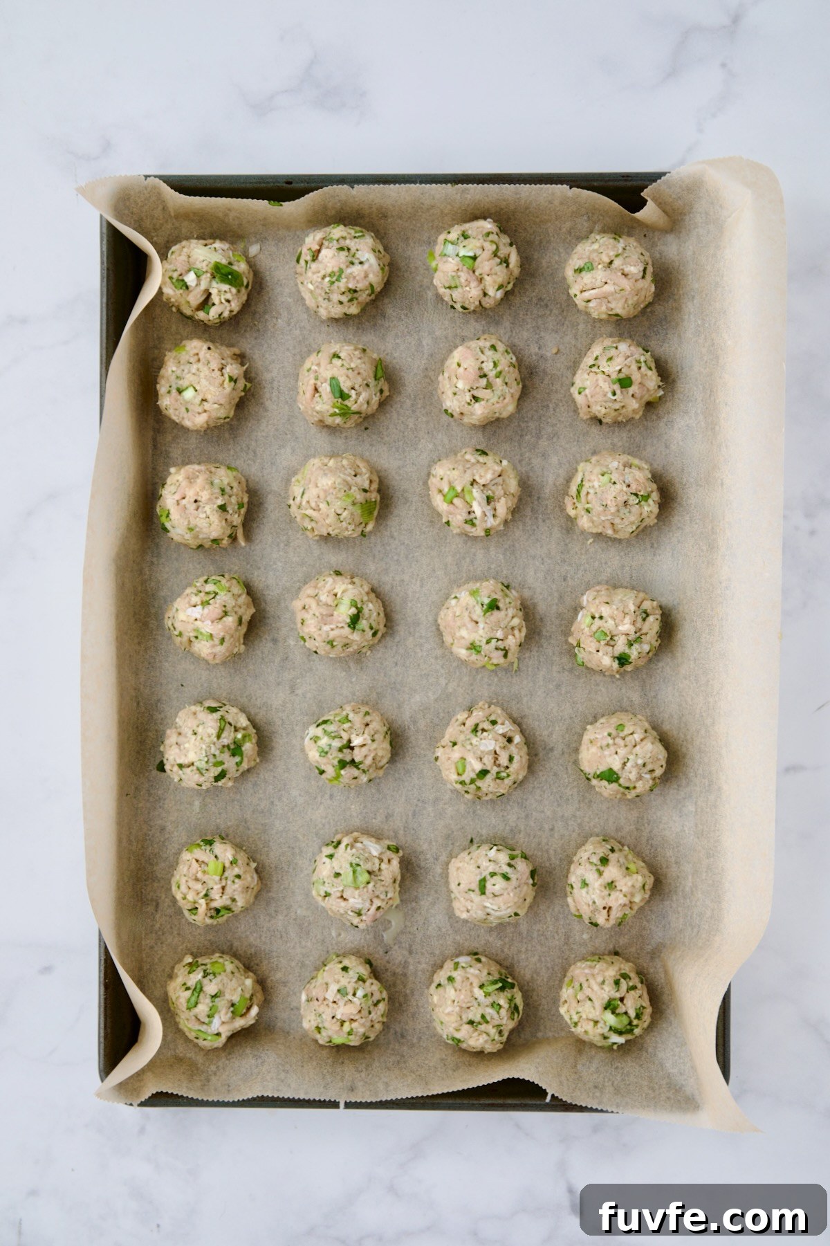 Asian-Style Turkey Meatballs with Ginger-Soy Glaze 8 Turkey meatballs on parchment paper lined baking sheet before being baked.