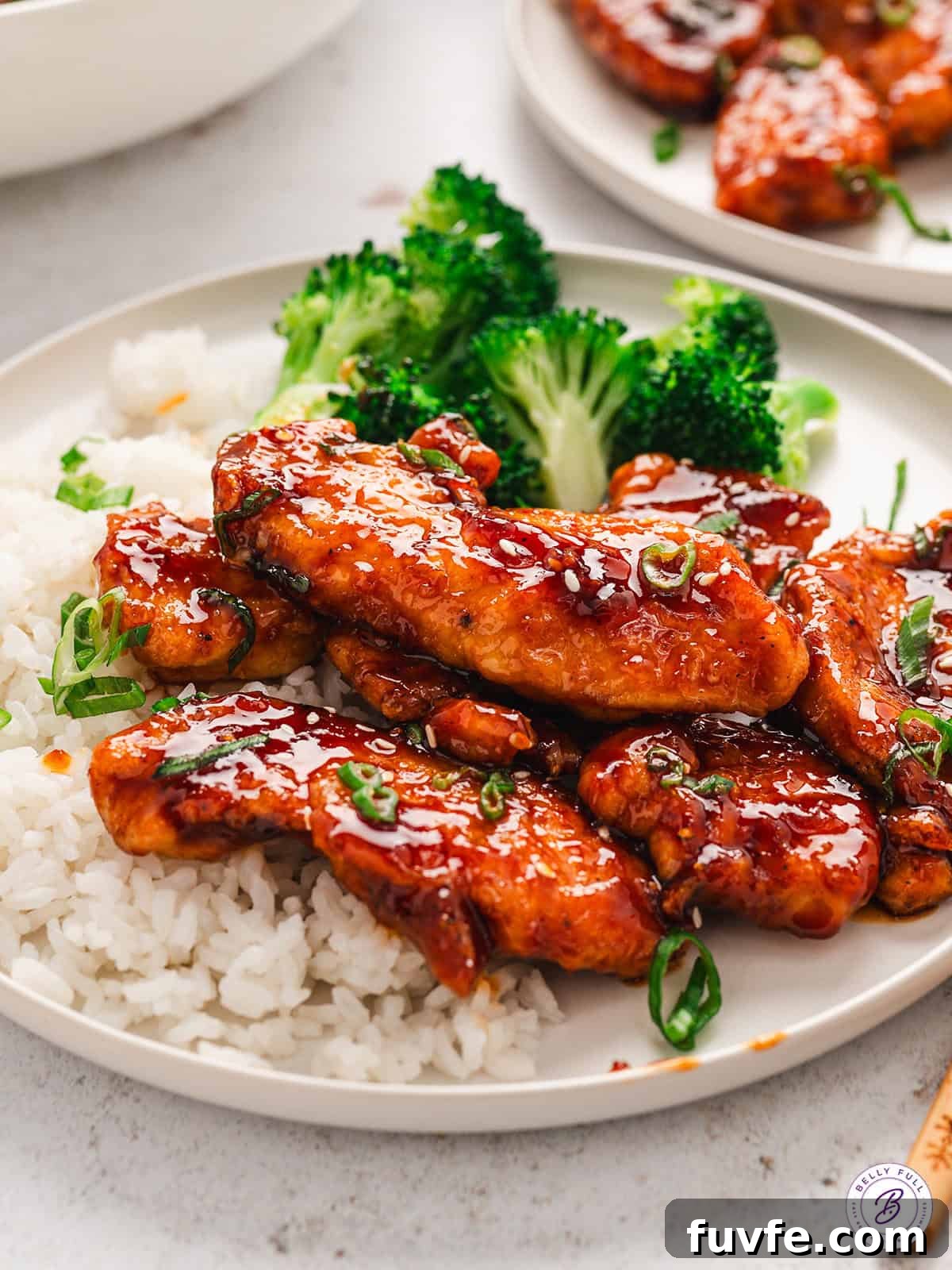 A plate of sweet sticky spicy chicken with rice and broccoli.