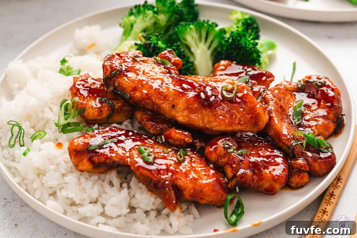 Sweet and spicy sticky chicken on a white plate with white rice and broccoli.