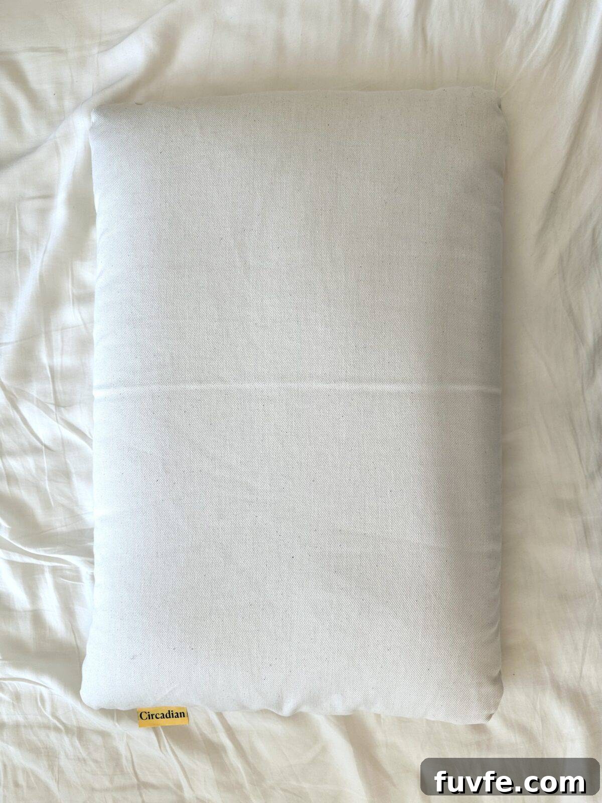 Top Non-Toxic Pregnancy and Organic Nursing Pillows for Moms 7 A plain white rectangular pillow with a small yellow brand tag rests on a rumpled white bedsheet.