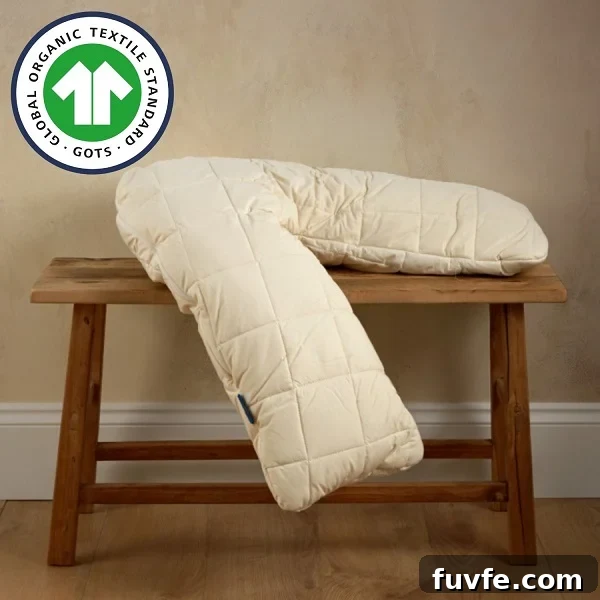 Top Non-Toxic Pregnancy and Organic Nursing Pillows for Moms 9 A cream-colored, quilted V-shaped pillow is draped over a rustic wooden bench in a minimalist setting, featuring a GOTS organic certification logo in the corner.