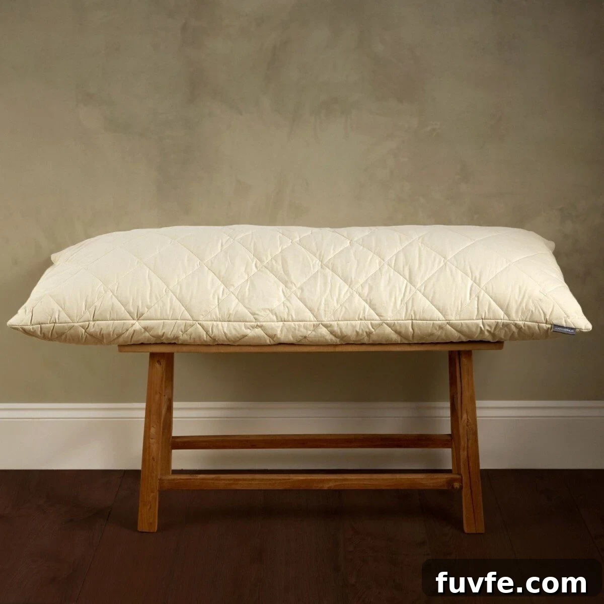 Top Non-Toxic Pregnancy and Organic Nursing Pillows for Moms 10 A long, cream-colored quilted pillow with a diamond pattern rests horizontally on a rustic wooden bench against a neutral, minimalist wall.