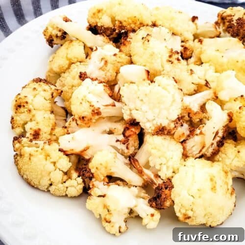 Crispy Air-Fried Cauliflower Recipes for Every Meal 10 Air fryer fried cauliflower florets served on a white plate, with a striped cloth and a garlic bulb in the background.