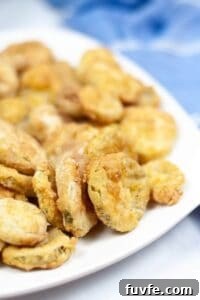 Crispy Air-Fried Cauliflower Recipes for Every Meal 8 A plate of golden-brown air fryer pickles sits on a white dish, with a blue cloth blurred in the background.