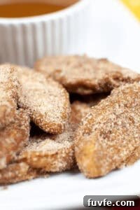 Crispy Air-Fried Cauliflower Recipes for Every Meal 9 A close-up of cinnamon sugar-coated air fried apple slices on a plate, with a white cup partially visible in the background.