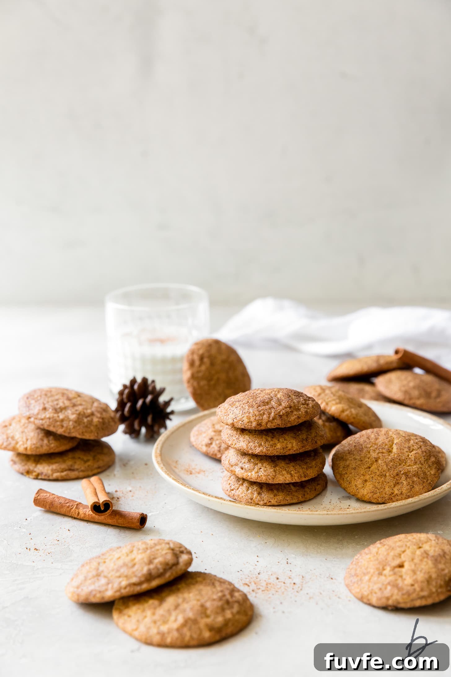 pumpkin snickerdoodles on a plate and around a plate with cinnamon sticks, milk glass behind plate