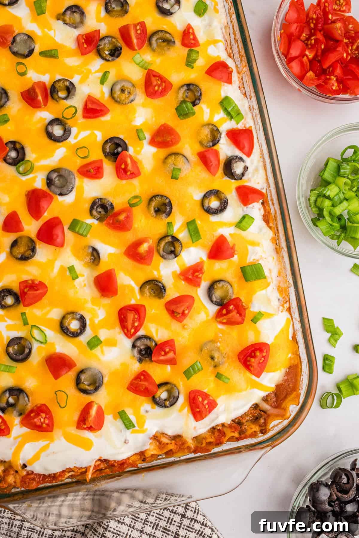 Overhead view of mexican taco lasagna topped with cheese, tomatoes, olives, and green onions.