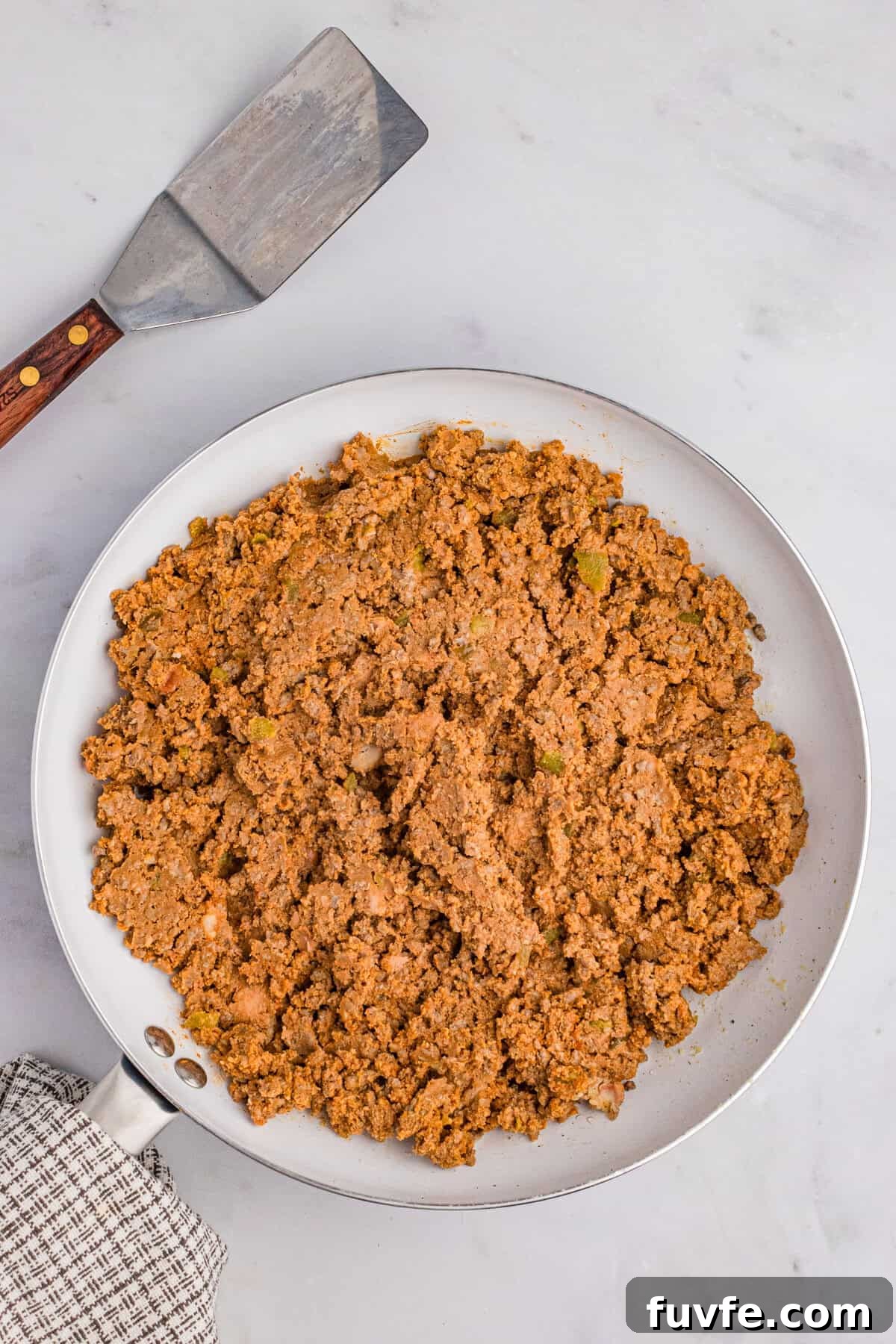 Seasoned taco meat with refried beans in a white skillet with a spatula nearby.