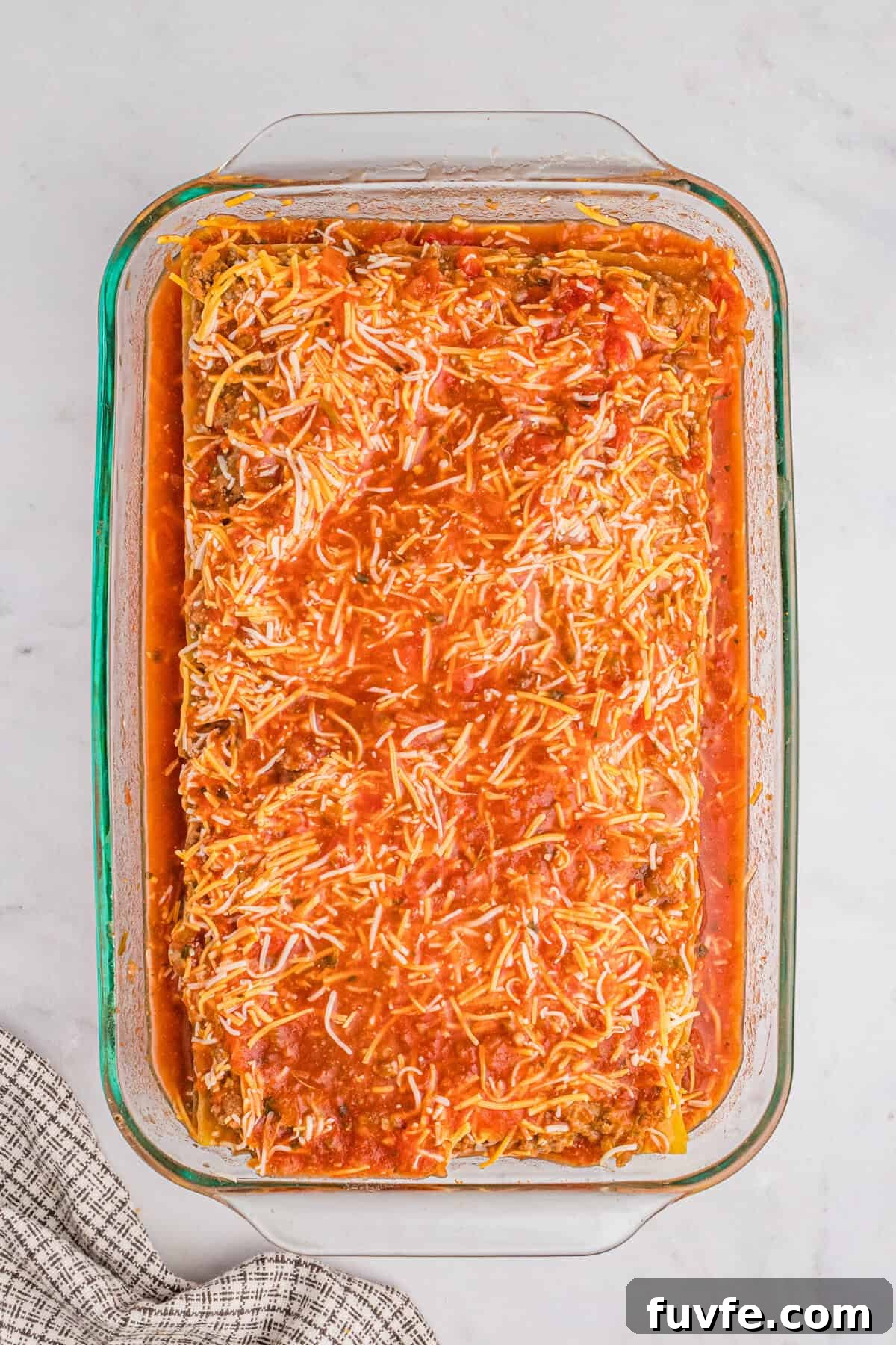 A glass baking dish filled with layered taco lasagna before baking, covered with red salsa.