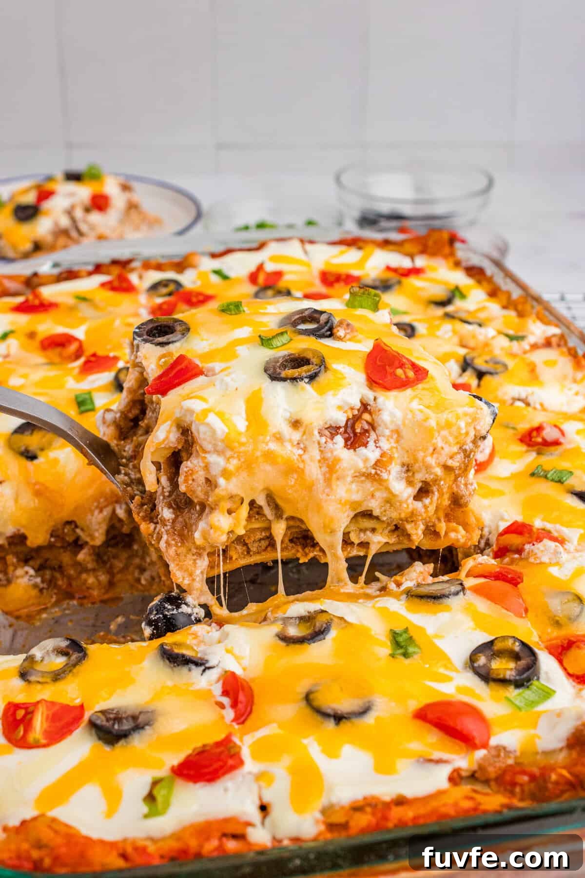 A cheesy slice of taco lasagna with lasagna noodles being lifted from a glass baking dish.