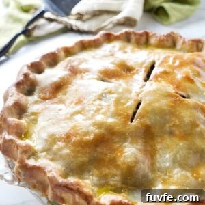 Golden-brown baked pie in a clear dish on white surface.