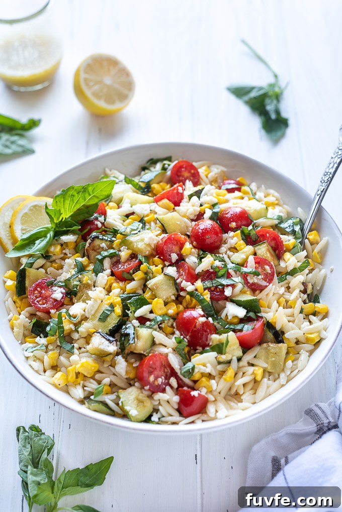 Summer orzo pasta salad in a bowl with a spoon nestled inside