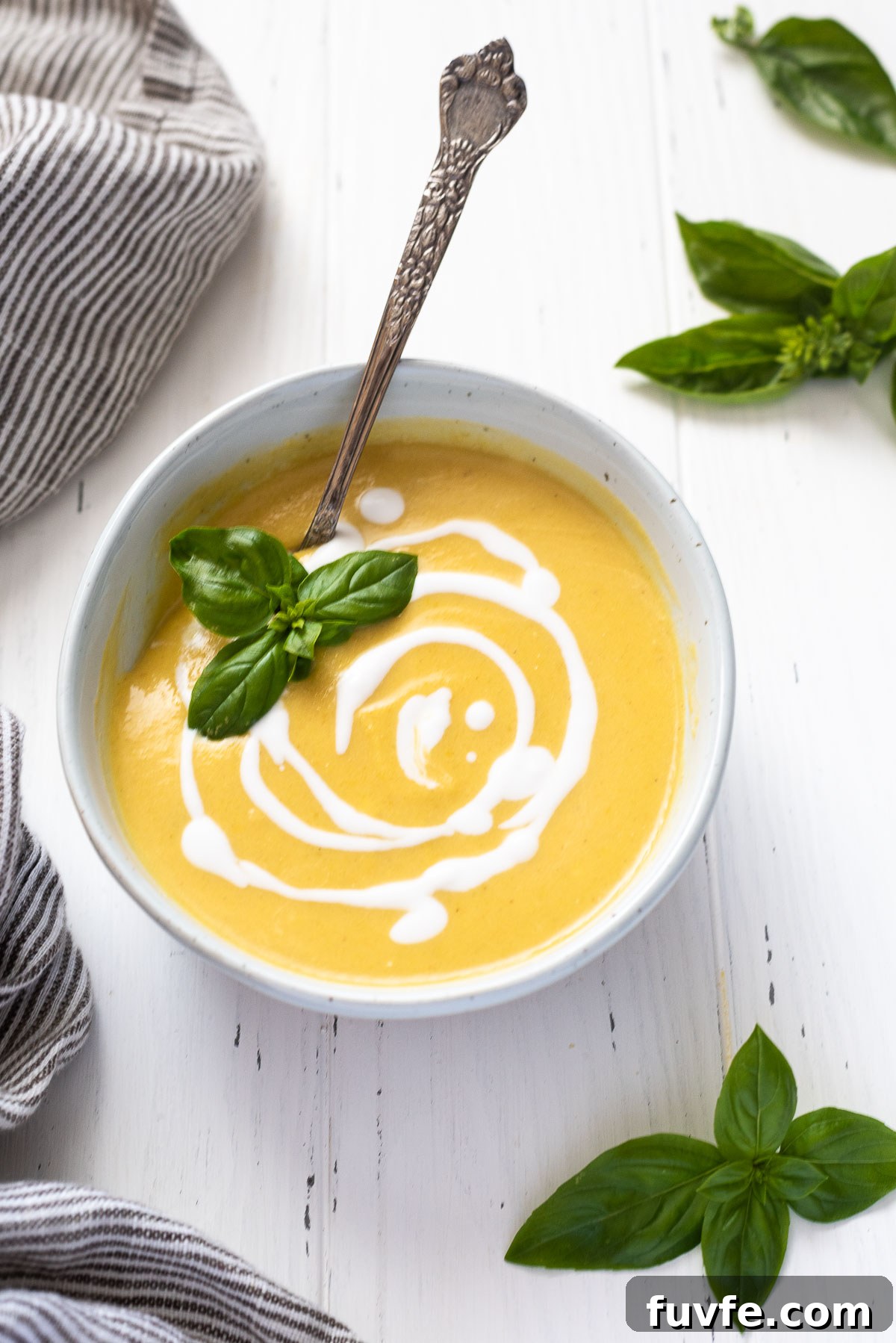 Bowl of summer squash soup with basil leaves on top and spoon inside