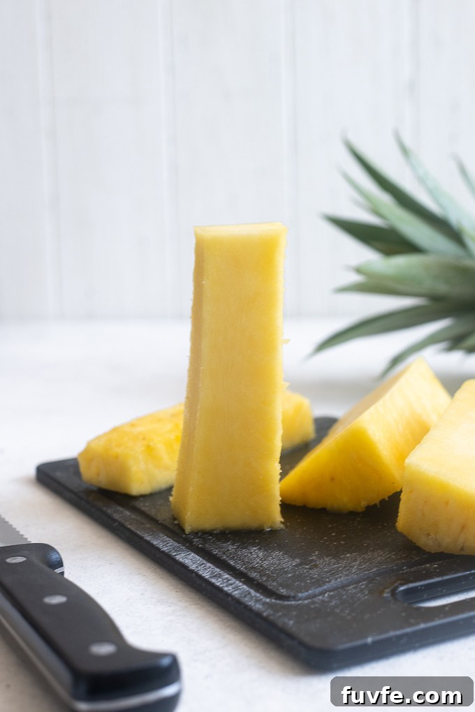 Pineapple core standing on cutting board with pineapple alongside.
