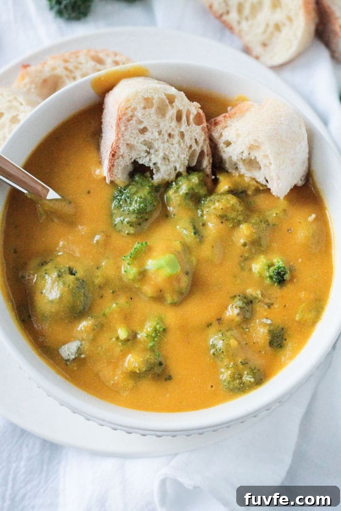 Bowl of Vegan Broccoli Cheese Soup. Metal spoon in the soup and one torn piece of crusty bread on the side.