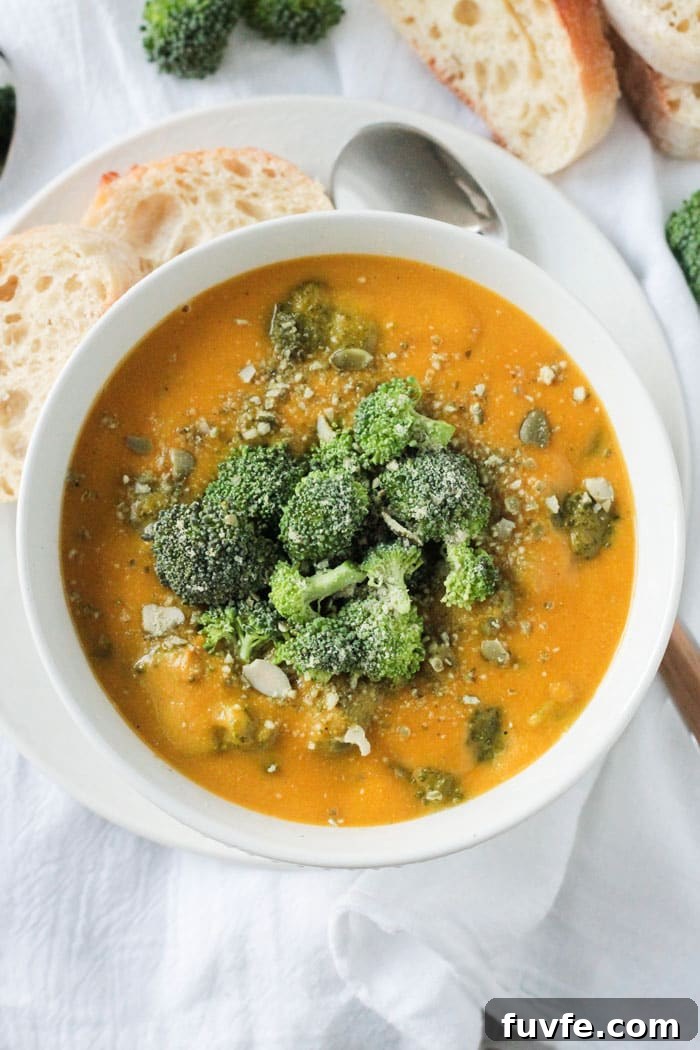 Vegan Broccoli Cheese Soup in a white bowl on a white plate. White dish cloth under the plate.