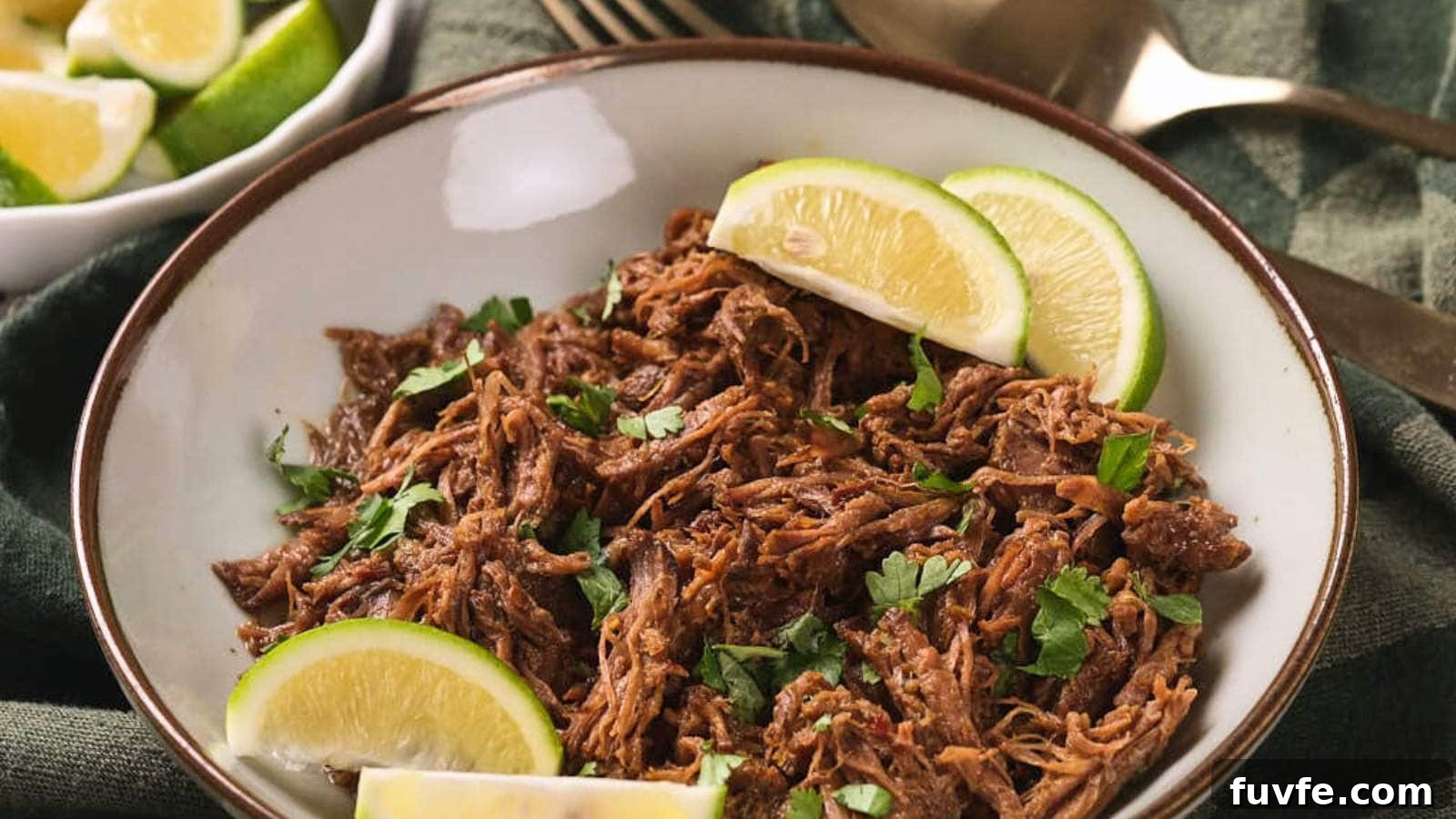 A plate of beef barbacoa garnished with chopped cilantro and lime wedges, placed on a green cloth.