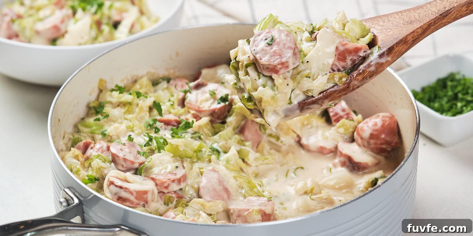 A skillet containing a creamy cabbage and sausage alfredo garnished with herbs.