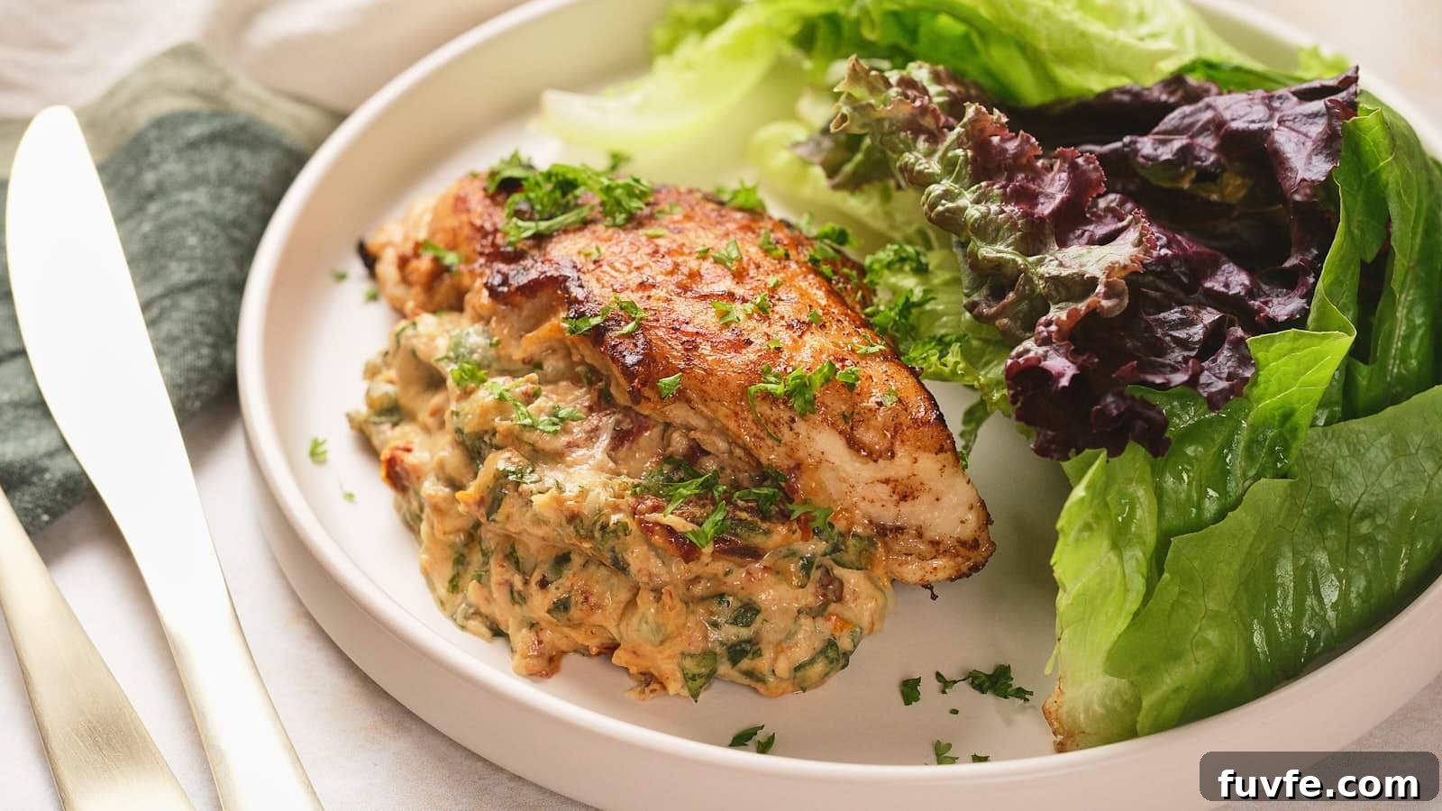 A plate with a cooked stuffed chicken breast garnished with herbs, served alongside fresh green and purple lettuce leaves.