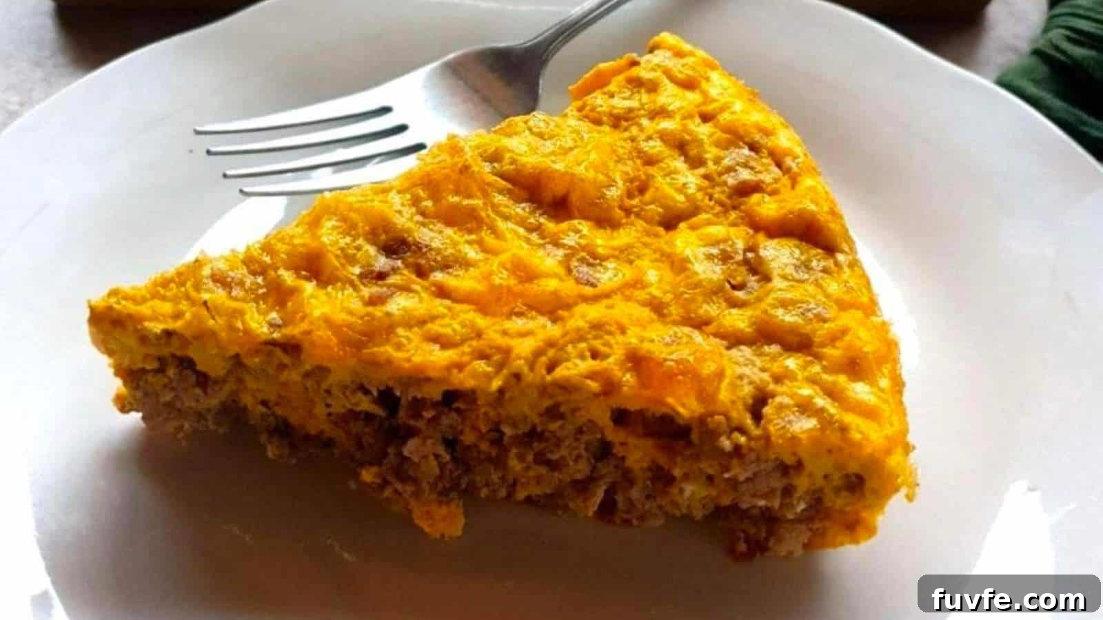 A slice of ground beef and egg casserole with a golden crust on a white plate, accompanied by a fork.